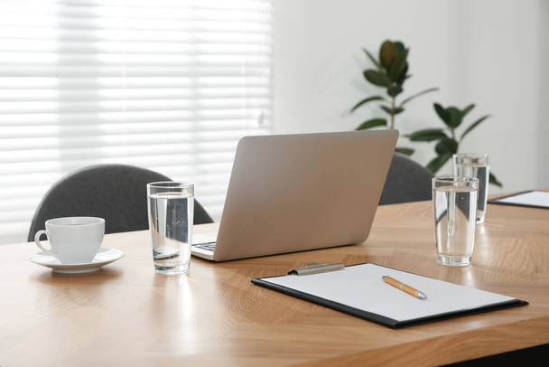 Modern laptop, glasses of water and clipboard on wooden table in conference room. Interior design - Photo, Image