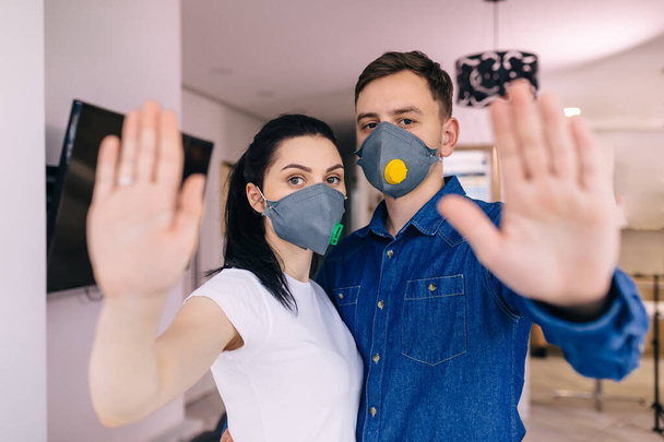 een man en een meisje met medische maskers op hun gezicht, staan met een uitgestoken hand en tonen een gebaar om het virus te stoppen. - Foto, afbeelding
