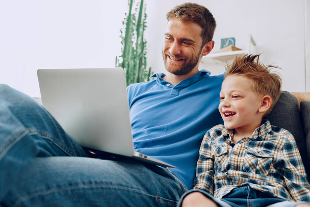 Father and son sitting on couch and watching something on laptop - Photo, Image