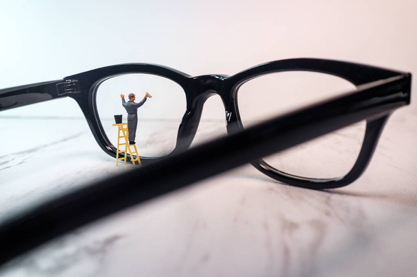 Γυαλιά οράσεως που καθαρίζονται από μικροσκοπικό ειδώλιο που συμβολίζει την καθαρή όραση - Φωτογραφία, εικόνα