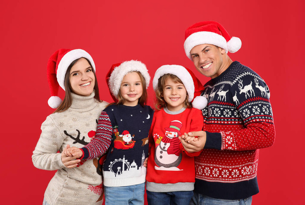 Family in Christmas sweaters and Santa hats on red background - Фото, изображение