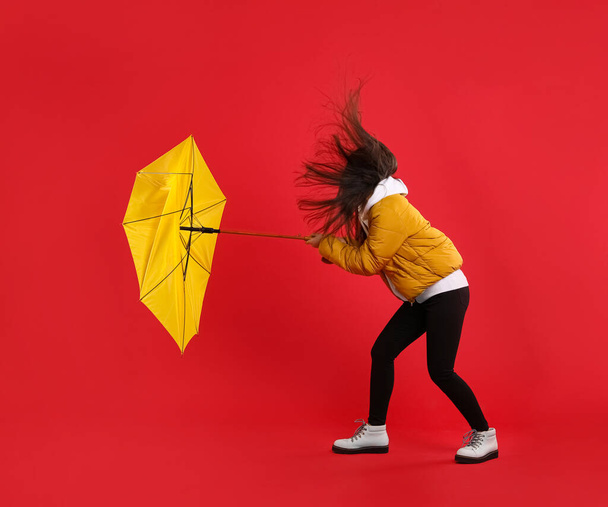 Woman with umbrella caught in gust of wind on red background - Foto, imagen