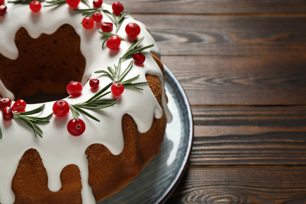 Traditional Christmas cake decorated with glaze, pomegranate seeds, cranberries and rosemary on wooden table, closeup. Space for text - Foto, Imagen