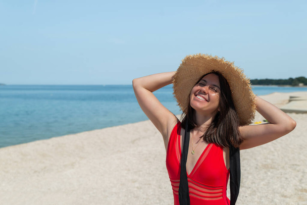 portret van jonge mooie vrouw in rood badpak op het strand. kopieerruimte - Foto, afbeelding