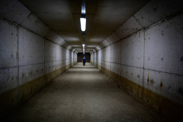 Un homme marche dans un passage souterrain. C'est un environnement sombre.. - Photo, image