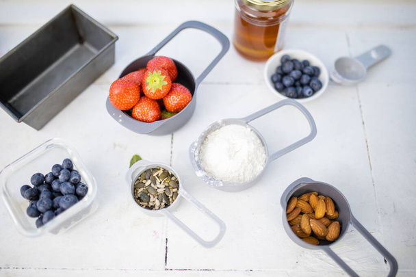 Berries, flour, and nuts in containers above white counter - Photo, Image