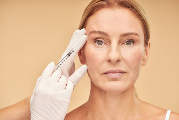Anti aging procedures. Beautiful mature woman receiving hyaluronic acid injection by beautician - Foto, afbeelding