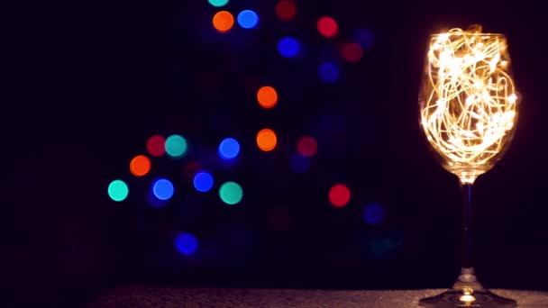 Cristallo champagne vetro decorato con ghirlanda dorata incandescente sul tavolo di Natale bokeh luci di sfondo. Cena romantica di Capodanno con coppia di vini bianchi innamorati. Magiche vacanze invernali atmosfera - Filmati, video