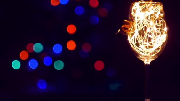 Kristall-Champagner-Glas mit goldenen leuchtenden Girlanden auf dem Weihnachtstisch Bokeh Lichter Hintergrund dekoriert. Romantisches Silvesterdinner mit einem verliebten Weißweinpaar. Magische Winterurlaubsatmosphäre - Filmmaterial, Video