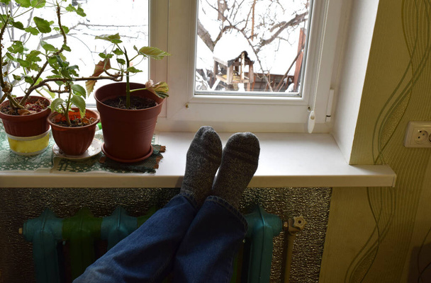 Erkek ayakları kışın pencerenin yanındaki radyatörde. - Fotoğraf, Görsel