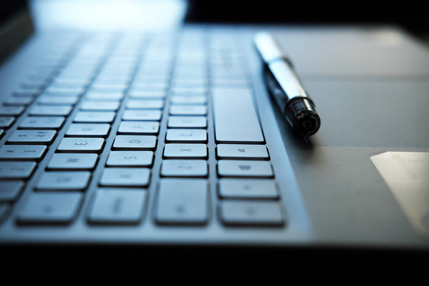 Πληκτρολόγιο και στυλό laptop - φωτογραφία που αντιπροσωπεύει την έννοια της απομακρυσμένης εργασίας με επιλεκτική εστίαση - Φωτογραφία, εικόνα