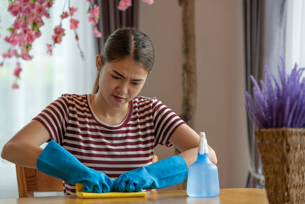Asiatische Hausfrau mit Handschuhen und Spray in der Hand wischt den Tisch im heimischen Wohnzimmer ab, Happy Putzkonzept - Foto, Bild