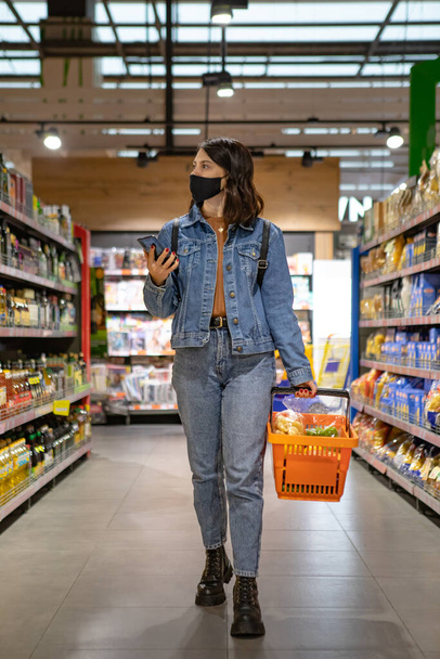 woman do grocery shopping checking list on the phone medical mask on the face covid - Foto, Imagen