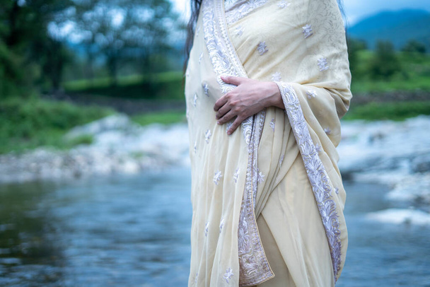 曇った雲と川の風景の前に伝統的な参照立って身に着けている美しいインドの若い女性モデル. - 写真・画像