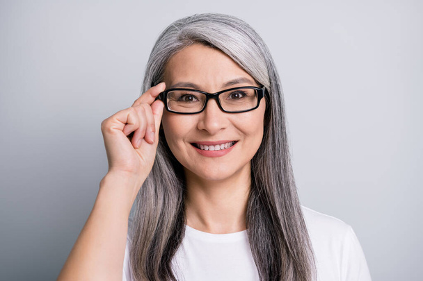 Photo of retired woman toothy smile look camera hold specs wear eyeglasses white t-shirt isolated grey color background - 写真・画像