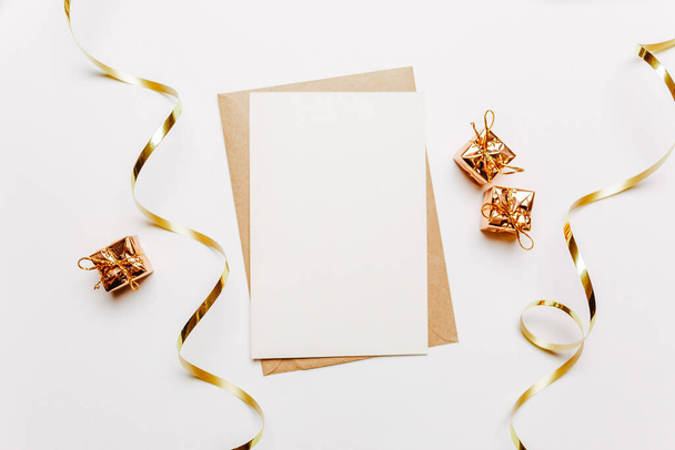 Nota en blanco con sobre, regalos y cinta de oro sobre fondo blanco - Foto, Imagen