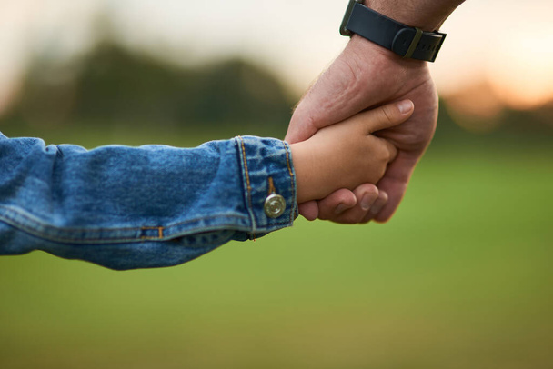Κοντινό πλάνο του μικρού κοριτσιού κρατώντας το χέρι του πατέρα, ενώ περνούν το χρόνο τους μαζί στο πράσινο πάρκο - Φωτογραφία, εικόνα