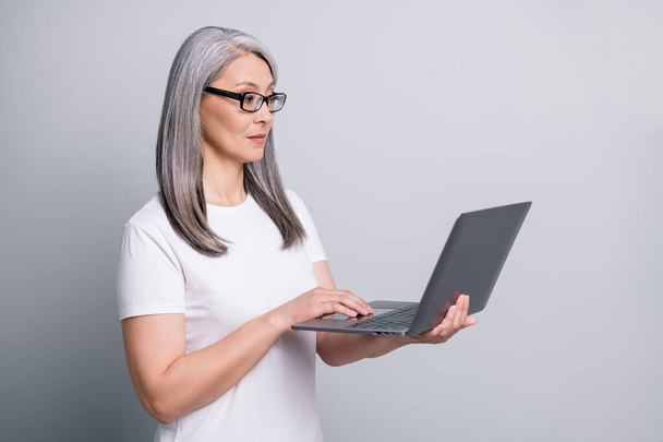 Profile photo of serious retired lady hold laptop look screen wear glasses white t-shirt isolated grey color background - Photo, Image