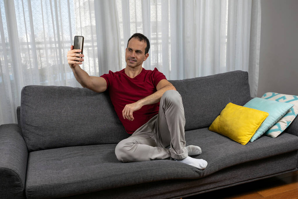 Dojrzały mężczyzna (44 lata) siedzi na kanapie, nosi skarpetki i robi sobie zdjęcie. - Zdjęcie, obraz