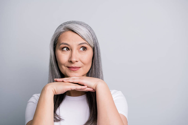 Photo portrait of curious old woman with grey hair keeping hands near chin looking at blank space isolated on grey color background - Foto, Imagem