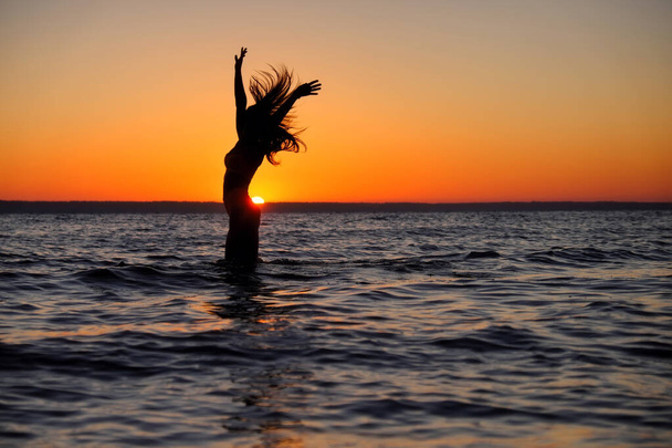 少女は海で泳いで、日没時に水に飛び込む。リラクゼーションと幸せな娯楽。夏休み.  - 写真・画像