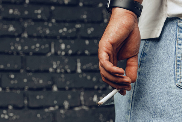 Male hand holding lit cigarette against black background - Foto, Imagen