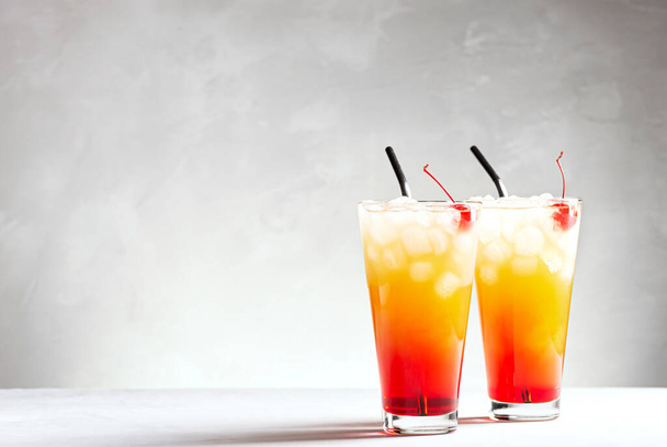 Two beautiful cocktails of tequila sunrise on a gray concrete background, horizontal orientation, selective focus, copy space. - Photo, Image