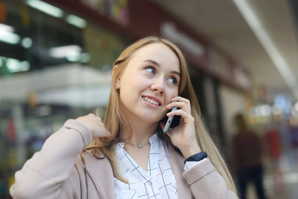 szczęśliwa długowłosa dziewczyna rozmawiająca przez telefon w opuszczonym centrum handlowym bez maski. - Zdjęcie, obraz