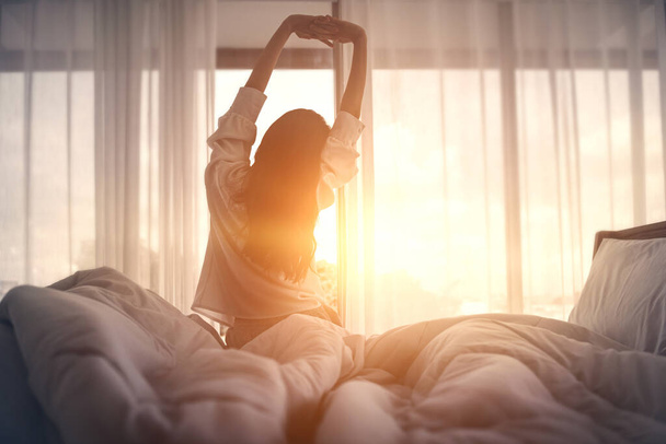 Женщина протягивает руки в постели после пробуждения утром, Концепция нового дня и радостные выходные. - Фото, изображение