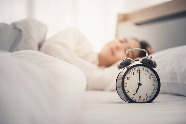 Young woman sleeping on bed with alarm clock in morning. - Φωτογραφία, εικόνα