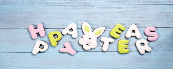 Happy Easter colorful lettering Happy Easter of ginger biscuits and cookies bunny on wooden blue background. Easter background or greeting card - Photo, Image
