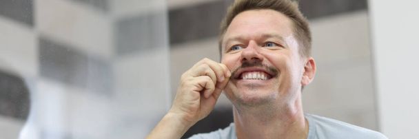 El hombre sonríe y sostiene su bigote frente al espejo - Foto, Imagen