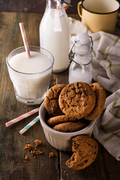 Double chocolate cookies with chips on a bowl and milk in glass on a rustic wood background, copy space - Fotoğraf, Görsel