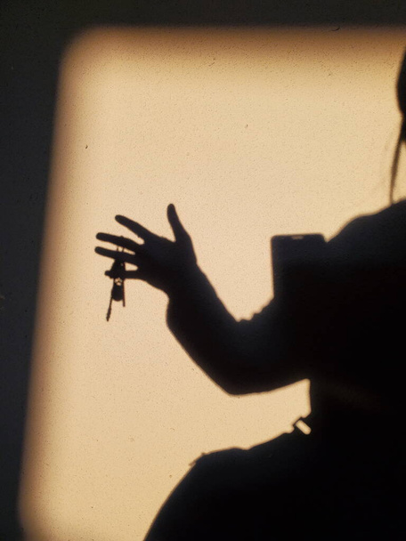 Γυναικεία σκιερά σιλουέτα με κλειδιά στο χέρι - Φωτογραφία, εικόνα