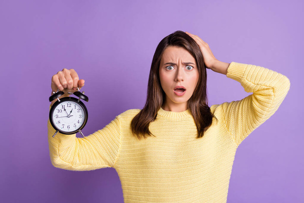 Photo portrait of upset woman running late holding black clock in one hand touching head hair isolated on vivid purple colored background - Foto, Imagen