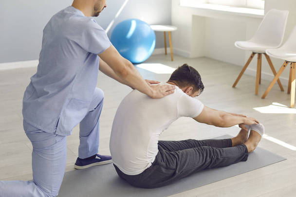 Side view arts helpt de patiënt te doen stretching oefeningen en yoga na het letsel. - Foto, afbeelding