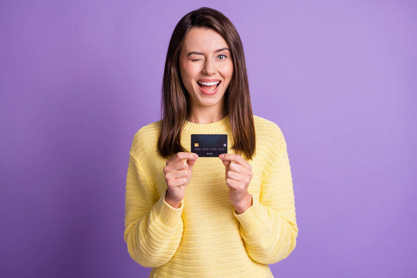 Foto-Porträt des hübschen Mädchens blinkt fröhlich zeigt Bank-Kreditkarte lächelnd tragen gelbe Kleidung isoliert auf lebendigen lila Farbhintergrund - Foto, Bild