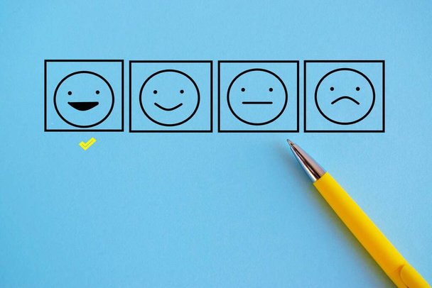 Klanttevredenheid happy feedback rating checklist en uitstekende zakelijke kwaliteit evaluatie concept met een controlerende glimlach emoticon gezicht pictogram close-up te bekijken. blauwe achtergrond, kopieer ruimte - Foto, afbeelding
