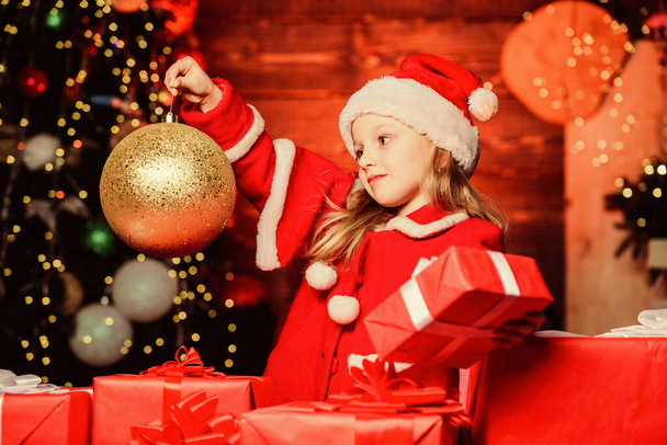 Bringing out holiday decoration for a festive atmosphere. Small child holding Christmas glitter ball decoration. Little girl looking at ornament ball decoration. Cute kid in xmas interior decoration - Zdjęcie, obraz