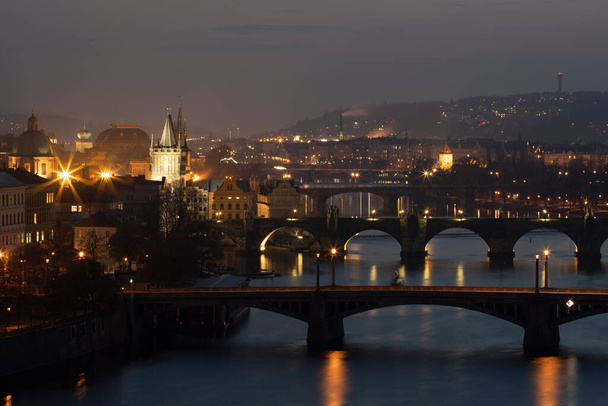 widok na Wełtawę i mosty na nim między mostami i Mostem Karola i otaczającej architektury i światła z ulicy światła w centrum Pragi po zachodzie słońca - Zdjęcie, obraz