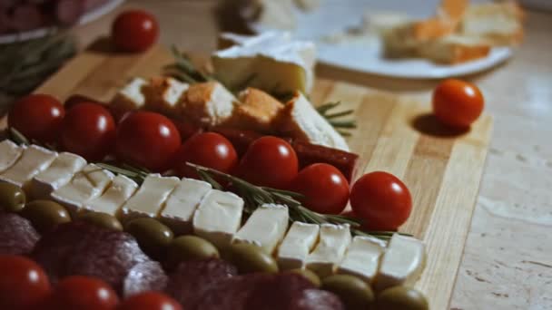 Flat lay of cheese and meat platter. Slices of cheese, smoked sausage, tomatoes, olives and rozmarin arranged in a shape of Christmas Tree. Food for Christmas holiday. Slowmotion - Footage, Video