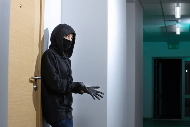 Thief broke into the apartment. House robbery by woman in a black jacket and black mask black gun and crowbar. Burglar in a mask. Thief in a mask trying to break into other people's house. - Photo, Image