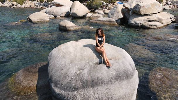 Egy hölgy áll egy nagy szikla előtt a tó körül. - Fotó, kép