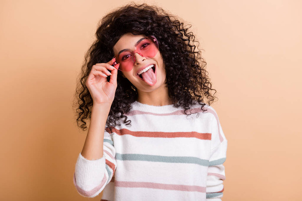 Photo of young excited crazy latin girl happy smile grimacing tongue out wear pink sunglass isolated over beige color background - Fotografie, Obrázek