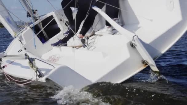 スローモーション撮影。白いヨットに乗って二人の女の子と男に座る彼らは手と足で帆を制御します - 映像、動画