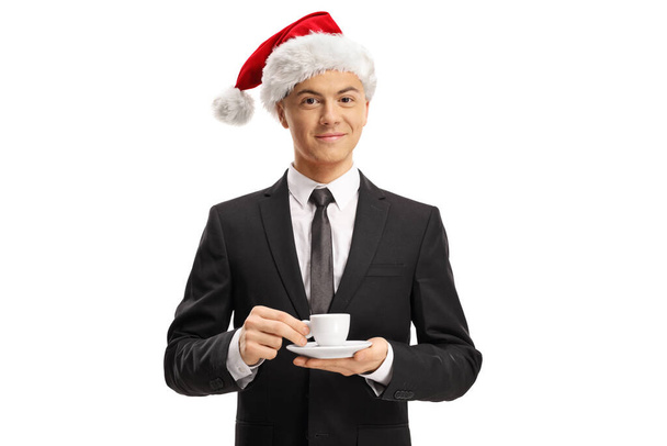 Young man in a suit wearing a santa hat and holding an espresso coffee cup isolated on white background - Foto, Imagem