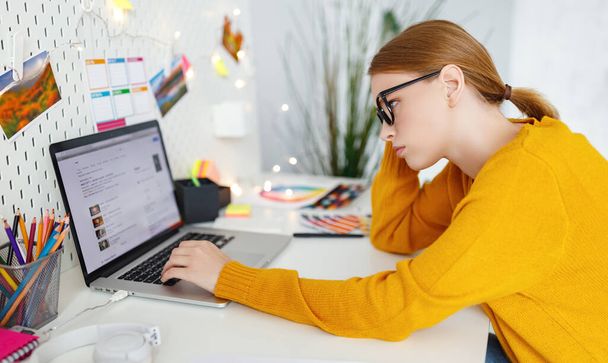 Vista laterale di donna freelance esausta seduta a tavola con netbook e appoggiata a portata di mano  - Foto, immagini