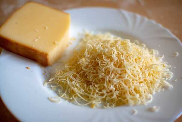 Egy darab sajt és egy halom reszelt sajt fehér tálcán. Szelektív fókusz. Közelkép. - Fotó, kép
