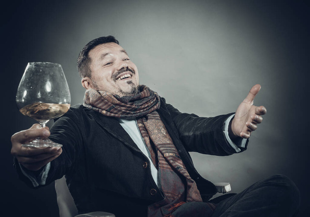 Solid cheerful man in kerchief sitting with glass of wine - Photo, image