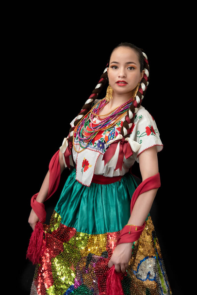 Donna latina vestita da poblana di porcellana con gonna ricamata in paillettes colorate, scialle rosso, fiocchi intrecciati e sfondo nero sorridente - Foto, immagini